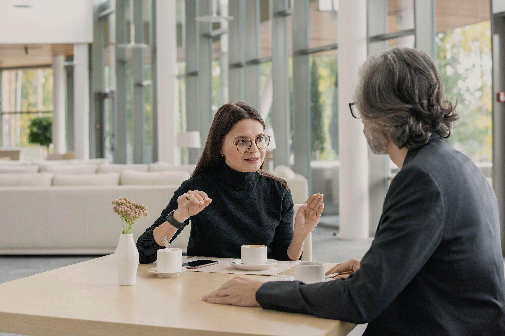 Two people in conversation at a table by a window